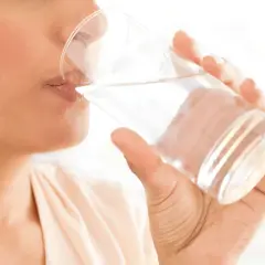Une personne boit un verre d'eau, un geste simple pour savoir comment bien s'hydrater et rester en forme.
