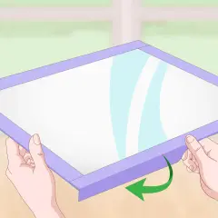 Manos sujetan un marco morado alrededor de una superficie blanca, mostrando cómo hacer una pizarra casera.