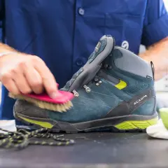 A person is cleaning a hiking boot with a brush, demonstrating how to maintain shoes.