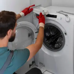 Mężczyzna w czerwonych rękawiczkach wyjmuje szufladę na proszek z pralki LG, która wyświetla błąd OE.