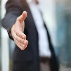 Biznesmen wyciąga rękę do uścisku, symbolizując partnerstwo i współpracę. Dowiedz się, jak założyć spółkę cywilną.