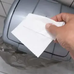 Dłoń z ręcznikiem papierowym zbliża się do kosza. Właśnie tu, gdzie wyrzucać ręczniki papierowe, by zachować czystość.