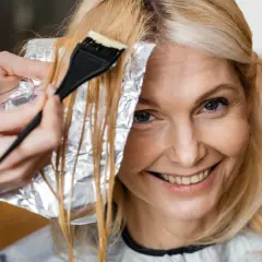Kobieta z uśmiechem na twarzy farbuje włosy. Jasny blond może postarzać, ale ona wygląda promiennie.