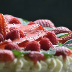 Pyszny tort dobosza, udekorowany malinami, truskawkami i listkami mięty, posypany srebrnymi kuleczkami.