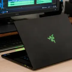 Czarny laptop Razer z podświetlanym logo, obok monitor z edytorem wideo i dysk sieciowy. Prawdopodobnie najdroższy komputer gamingowy na świecie.