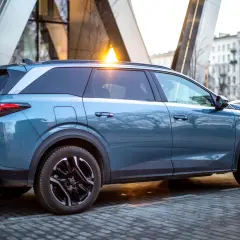 Niebieski Peugeot 5008 na tle nowoczesnej architektury. Wiele osób szuka peugeot 5008 opinie przed zakupem.