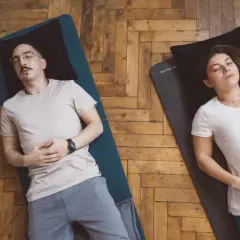 Un couple pratique la respiration profonde technique sur des tapis de yoga. Ils sont allongés sur le dos, les yeux fermés, les mains sur le ventre.