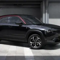Czarna Mazda MX-30 z czerwonym dachem, prezentująca swoje kompaktowe mazda mx 30 wymiary, stoi przed betonową ścianą z numerem 80.