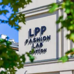 Napis LPP FASHION LAB COTTON na jasnym budynku, częściowo zasłonięty przez liście.