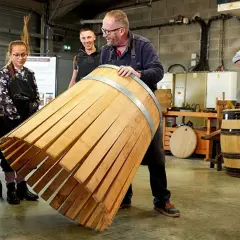 Visite tonnellerie Bourgogne : un maître tonnelier montre un fût en cours de fabrication à des apprentis.