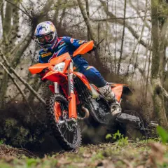 Piloto en una KTM 490 Adventure derrapando en un sendero boscoso, levantando barro.