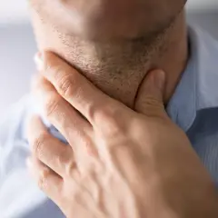 Mężczyzna dotyka szyi, odczuwając ból gardła po zimnym napoju.