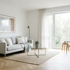 Jasny salon z szarą kanapą, szklanym stolikiem i krzesłem. Idealny przykład home stagingu, który podkreśla przestronność i styl.