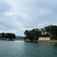 La isla de San Simón, con su casa de tejado naranja y frondosos árboles, se alza sobre el agua serena bajo un cielo nublado.