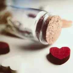 Cuore rosso vicino a una bottiglia tappata, simbolo di innamoramento e amore.