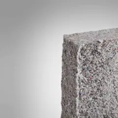 Bloque de material aislante grisáceo, similar a fibra de vidrio triturada. Evitar respirar estas partículas para prevenir consecuencias.