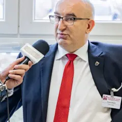 Mężczyzna w garniturze i czerwonym krawacie udziela wywiadu z mikrofonem Radia Eska.