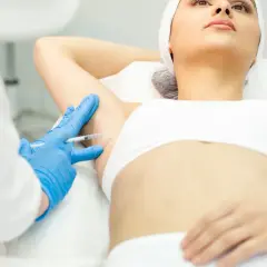 Zabieg botoks pod pachy. Lekarz w niebieskich rękawiczkach podaje zastrzyk.