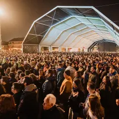 Multitudinaria asistencia al concierto astillero hoy bajo una gran carpa. La gente disfruta de la música y el ambiente nocturno.