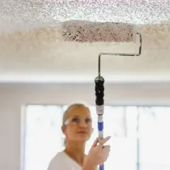 Donna imbianca il soffitto con un rullo, un modo semplice per rinnovare casa.