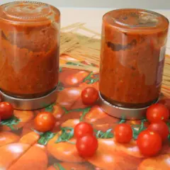 Zwei Gläser mit hausgemachtem tomaten sugo stehen neben Spaghetti. Frische Kirschtomaten zieren die Serviette mit Tomatenmuster.
