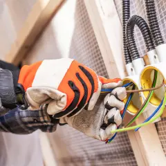 Ręce w rękawicach montują puszki elektryczne. To etap prac, który wpływa na to, ile kosztuje założenie instalacji elektrycznej w domu.