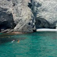 Gente nadando y haciendo snorkel en las aguas cristalinas de la cala puente Almería, rodeada de imponentes acantilados rocosos.