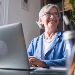 Lächelnde Frau am Laptop, die überlegt, wie sie Rente beziehen und vollzeit arbeiten kann, ohne die Steuerklasse zu ändern.