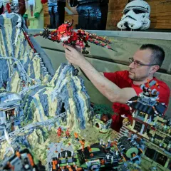 Mann mit Brille platziert roten Drachen in einem riesigen Lego-Set mit den meisten Teilen, das eine Berglandschaft mit Achterbahn und Gebäuden zeigt.