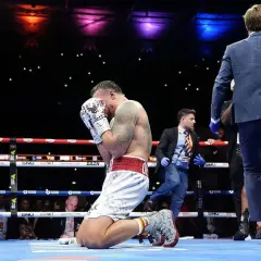 A boxer kneels in the ring, head in hands, after a tough fight. The Dubois vs Usyk bout ends with a somber moment.