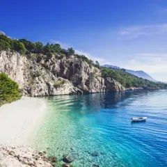 Kamienista plaża w Chorwacji z krystalicznie czystą wodą i łodzią na morzu.