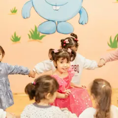 Dzieci trzymają się za ręce w kółku na tle ściany z rysunkiem niebieskiego królika.