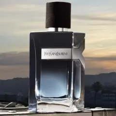 Elegancka butelka Y Yves Saint Laurent Y 100ml na tle zachodzącego słońca nad miastem.