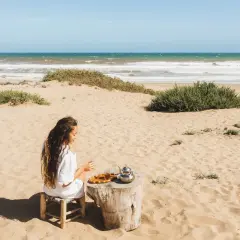 Kobieta pije herbatę na piaszczystej plaży w Tunezji, z widokiem na ocean.