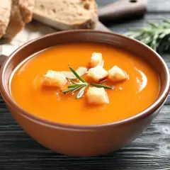 Aksamitny zupa krem z batatów, udekorowana grzankami i rozmarynem, podana z chlebem i pestkami dyni.