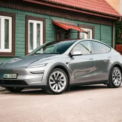Srebrny Tesla Y stoi przed zielonym domem. Zastanawiasz się, ile koni ma ten model?