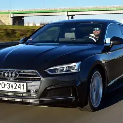 Czarny Audi A5 2025 z kierowcą w okularach przeciwsłonecznych jedzie po autostradzie.