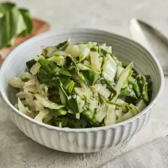 Schüssel mit gedünstetem Mangold, perfekt für ein einfaches Mangold Rezept. Frische Blätter liegen daneben.