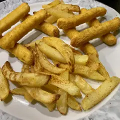 Ein Teller mit knusprigen belgischen Pommes, einige dick geschnitten, andere als Stäbchen frittiert.