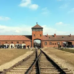 Brama obozowa Auschwitz I z wieżą, tory kolejowe prowadzące do niej. Zwiedzający zastanawiają się, ile trwa zwiedzanie Auschwitz, by poznać historię.