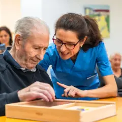 Un homme âgé participe à un atelier sensoriel, guidé par une aide-soignante attentive.