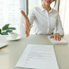 Bizneswoman wyciąga rękę do uścisku nad dokumentem "CONTRACT". Może to być umowa, wykreślenie hipoteki lub inny ważny wpis.