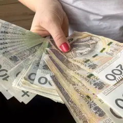 Dłoń trzyma wachlarz polskich banknotów 100 i 200 zł. To spory pensum gotówki, które można przeznaczyć na różne wydatki.