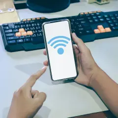 Dłoń trzyma smartfon z ikoną Wi-Fi. Dowiedz się, jak sprawdzić częstotliwość Wi-Fi w telefonie, aby zoptymalizować połączenie.