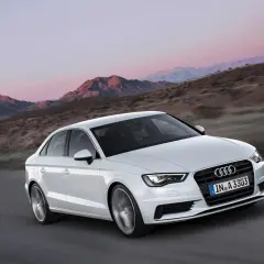 Białe Audi A3 jedzie po drodze w górach. Jego lekka konstrukcja i dynamiczny wygląd podkreślają jego sportowy charakter.