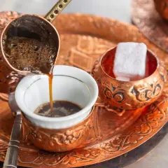 Frisch aufgebrühter, bester türkischer Kaffee fließt aus einer Kupferkanne in eine kleine Tasse. Daneben liegen süße Loukoum-Würfel.