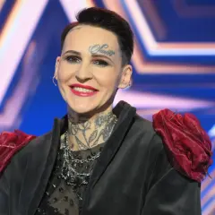 Agnieszka Chylińska z tatuażami na twarzy i szyi, w czarnej marynarce z czerwonymi ozdobami na ramionach.
