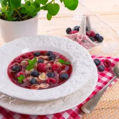 Pyszna zupa owocowa z malinami, borówkami i makaronem w kształcie motylków, udekorowana miętą.