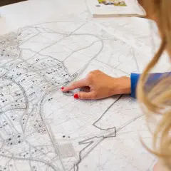 Kobieta analizuje szczegółowy plan zagospodarowania przestrzennego, wskazując palcem konkretny obszar na mapie.