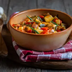 Aksamitne leczo z kurczakiem w glinianej misie, ozdobione rozmarynem. Obok drewniana łyżka i czosnek.